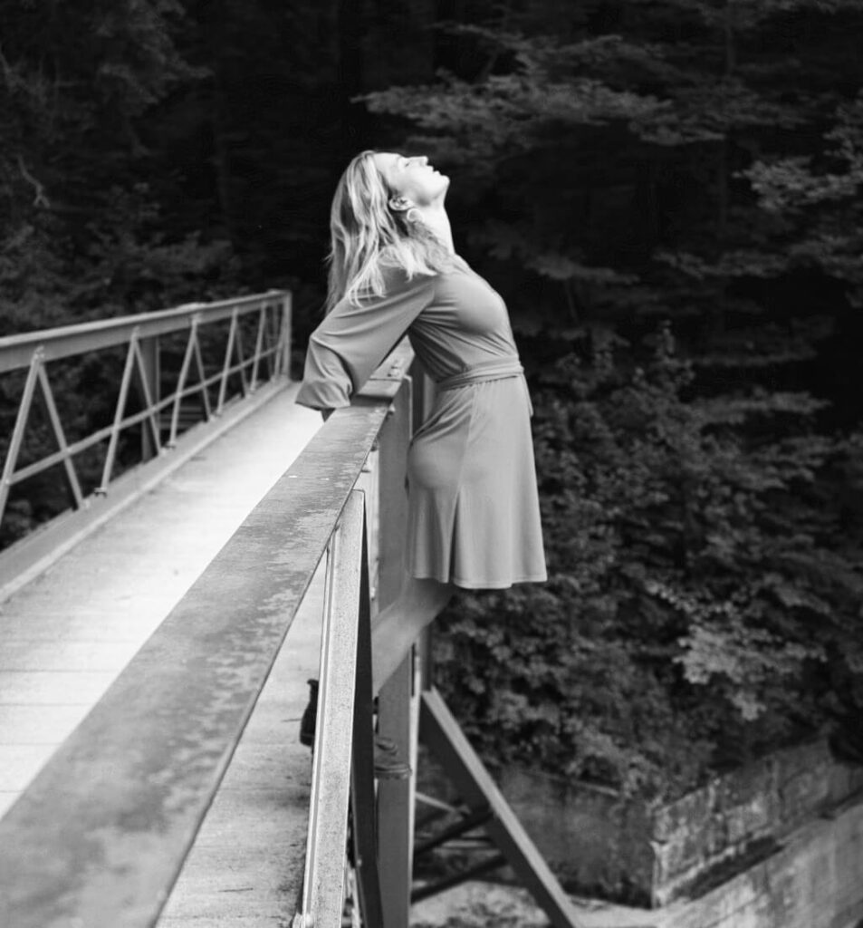 Frau steht in einer Pose vor einem Brückengeländer